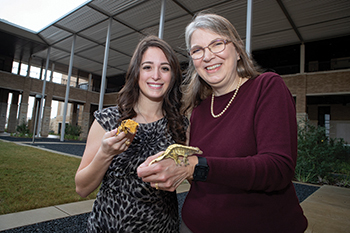 a female student and a female faculty member pose with reptiles in the VBEC courtyard