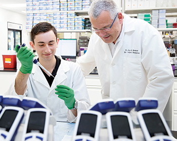 a male researcher mentors a male trainee as he pipettes a sample