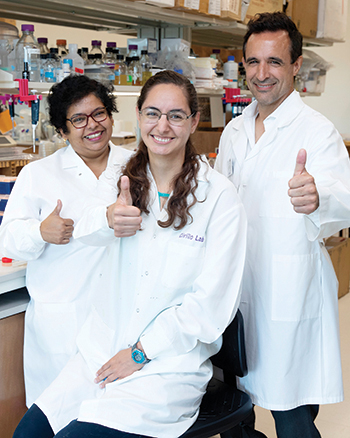 Three researchers give the thumbs up sign while posing for the camera in the lab
