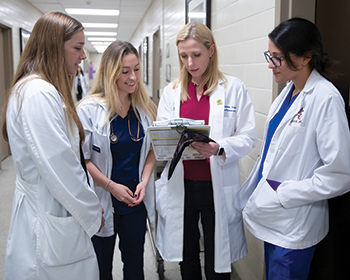 three female students and a female clinician review a chart in the hospital hallway